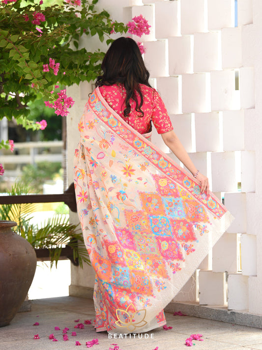 Woman in a floral saree standing outdoors with plants and flowers in the background