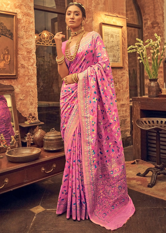 Woman in a pink saree with intricate patterns standing in an indoor setting.