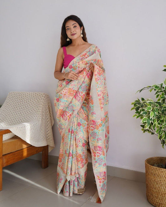 Woman wearing a floral saree in a room with a wooden chair and plant.
