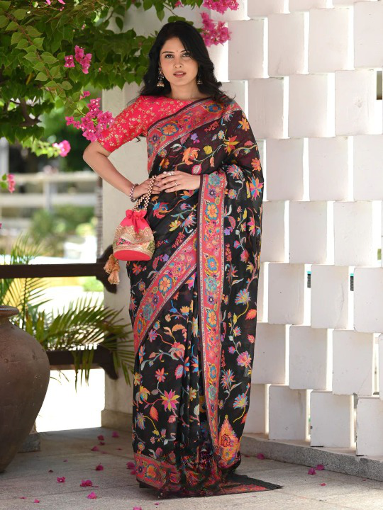 Woman wearing a black floral saree with a colorful border in an outdoor setting.