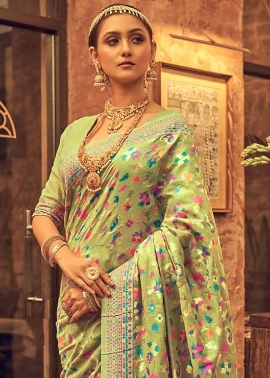 Woman in a traditional green saree with floral patterns and gold jewelry indoors.