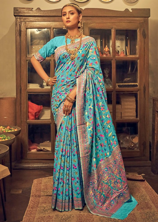 Woman in a blue saree with floral patterns in a room with wooden furniture.