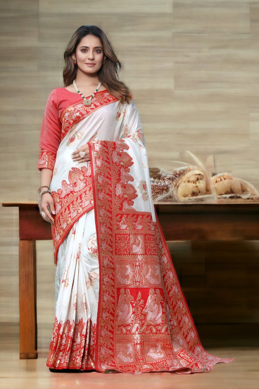 Woman wearing a white saree with red patterns and a red blouse, standing in front of a wooden table.